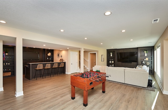 game room with light hardwood / wood-style flooring, a textured ceiling, and indoor bar