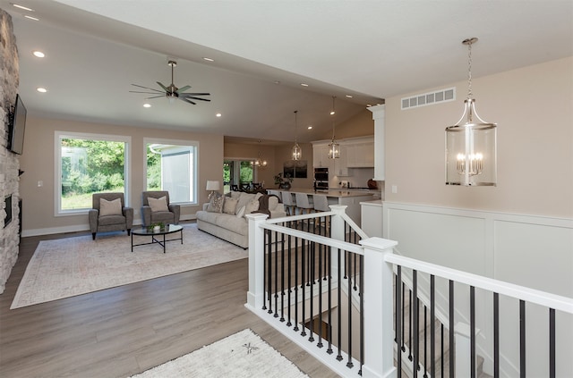 living room featuring hardwood / wood-style flooring, ceiling fan with notable chandelier, and vaulted ceiling