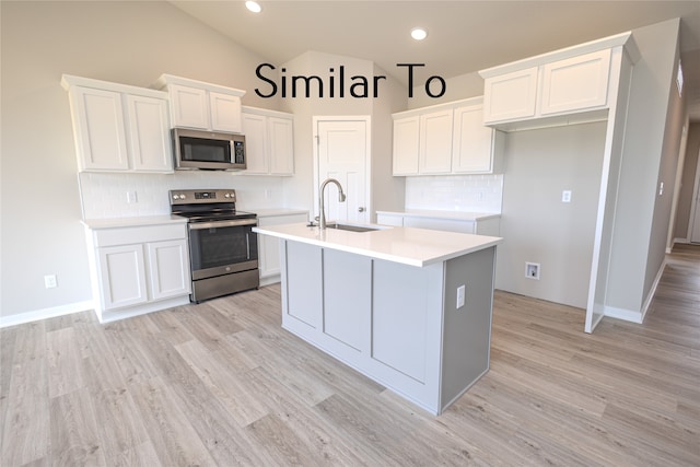 kitchen with sink, appliances with stainless steel finishes, white cabinetry, and an island with sink