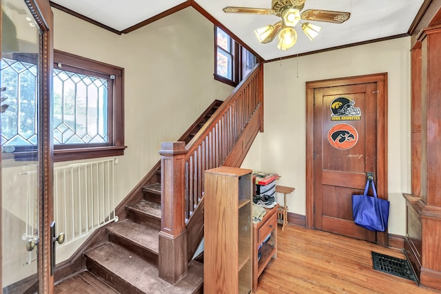 stairs featuring crown molding, hardwood / wood-style floors, a healthy amount of sunlight, and ceiling fan