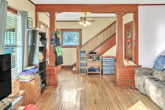 living room with ceiling fan, decorative columns, ornamental molding, and light wood-type flooring