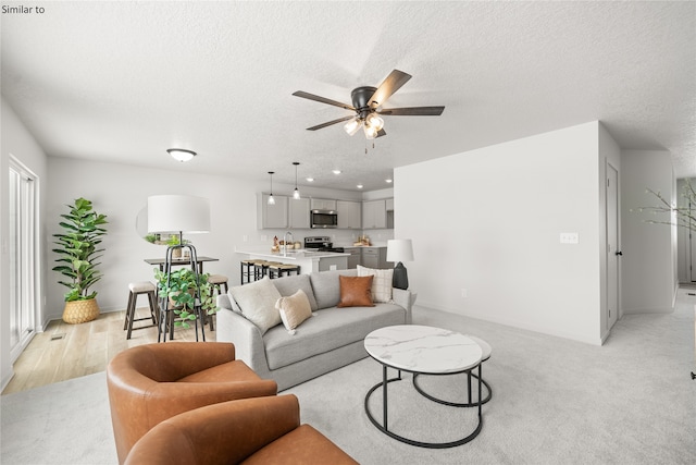 living room featuring ceiling fan, a textured ceiling, sink, and light wood-type flooring