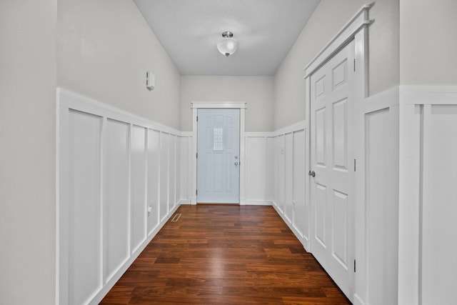 doorway to outside featuring wainscoting, dark wood finished floors, and a decorative wall