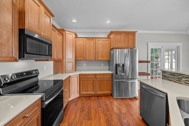 kitchen featuring brown cabinetry, crown molding, light wood finished floors, stainless steel appliances, and light countertops