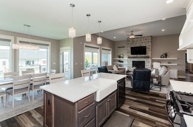 kitchen with stainless steel gas stove, dark wood-type flooring, dark brown cabinets, sink, and decorative light fixtures