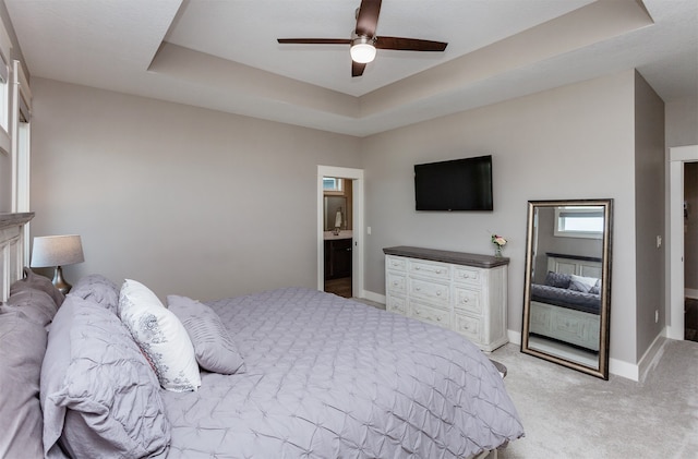 carpeted bedroom featuring a raised ceiling, ensuite bathroom, and ceiling fan