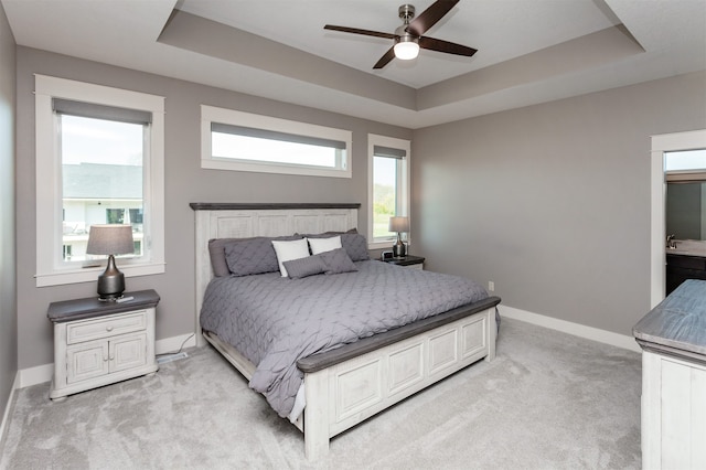 bedroom with ceiling fan, light carpet, and a tray ceiling