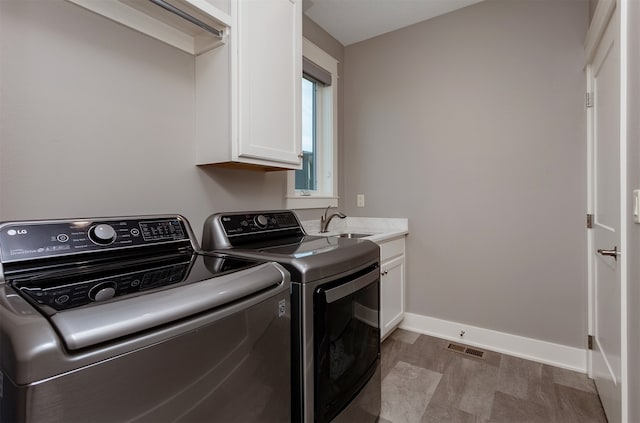 laundry room featuring sink, washing machine and clothes dryer, and cabinets