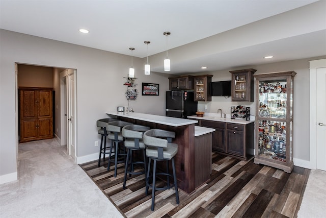 bar with sink, dark brown cabinets, black fridge, decorative light fixtures, and dark wood-type flooring