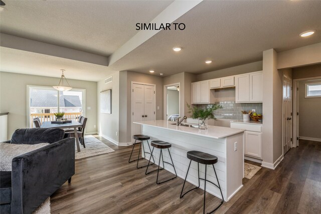 kitchen with backsplash, white cabinetry, hanging light fixtures, and a kitchen island with sink