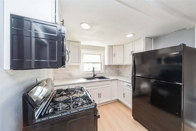 kitchen with white cabinetry, black appliances, light countertops, and a sink