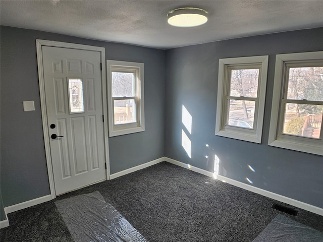 foyer with baseboards, visible vents, dark colored carpet, and a textured ceiling