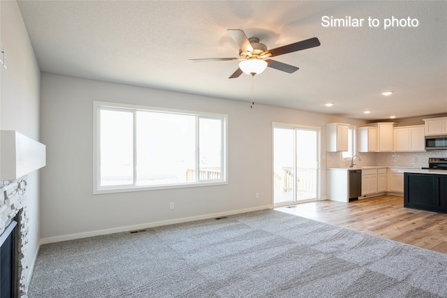 unfurnished living room featuring sink, ceiling fan, a textured ceiling, a fireplace, and light hardwood / wood-style floors