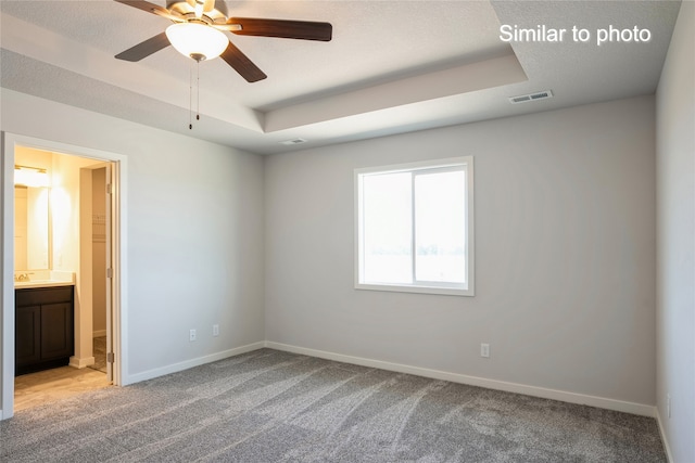 carpeted spare room with ceiling fan, a textured ceiling, and a tray ceiling