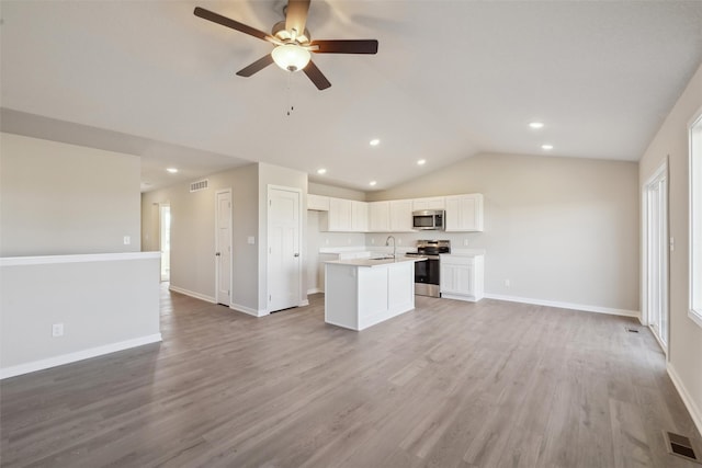 kitchen with light hardwood / wood-style flooring, appliances with stainless steel finishes, a kitchen island with sink, white cabinets, and vaulted ceiling