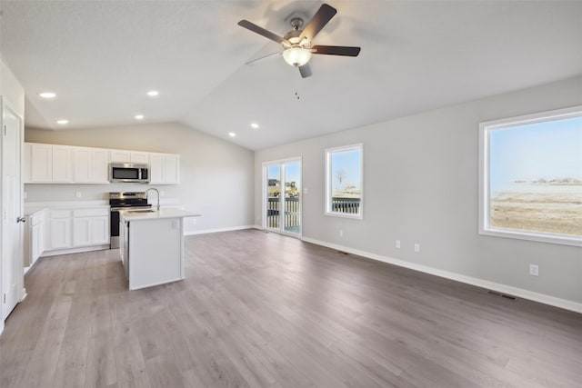 kitchen featuring vaulted ceiling, white cabinets, light hardwood / wood-style floors, stainless steel appliances, and a center island with sink