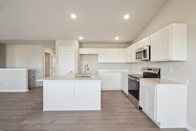 kitchen with appliances with stainless steel finishes, an island with sink, sink, white cabinets, and light wood-type flooring