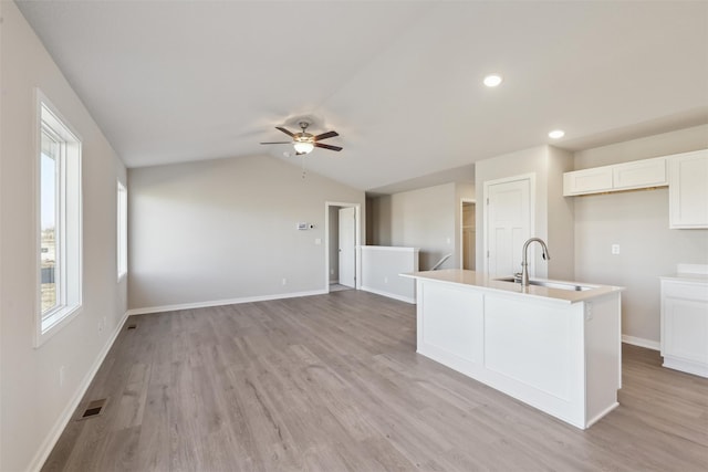 kitchen featuring sink, white cabinetry, light hardwood / wood-style floors, an island with sink, and vaulted ceiling