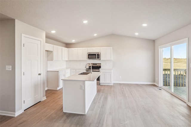 kitchen with a center island with sink, appliances with stainless steel finishes, light wood-type flooring, vaulted ceiling, and white cabinets