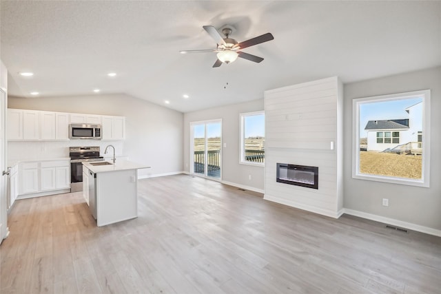 kitchen with white cabinets, lofted ceiling, stainless steel appliances, a large fireplace, and a kitchen island with sink