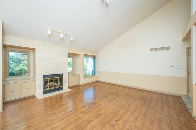 unfurnished living room with a tile fireplace, track lighting, light hardwood / wood-style floors, and plenty of natural light