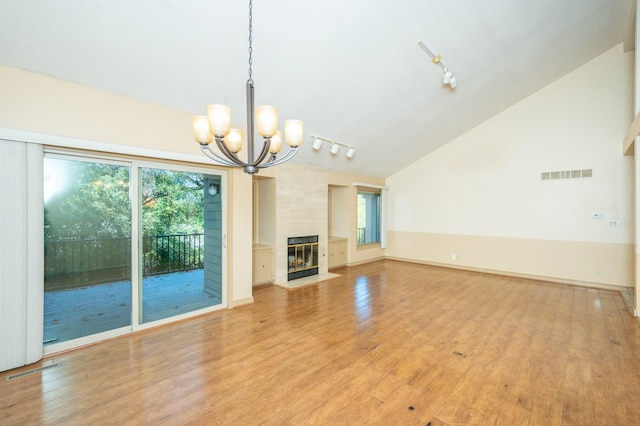 unfurnished living room with light wood-type flooring, visible vents, track lighting, a large fireplace, and lofted ceiling