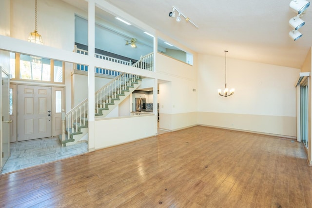 unfurnished living room featuring track lighting, an inviting chandelier, wood finished floors, and stairs