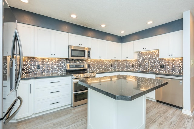 kitchen with a center island, light wood-type flooring, appliances with stainless steel finishes, white cabinets, and a sink