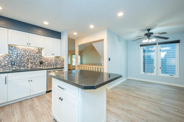 kitchen with decorative backsplash, light wood-style flooring, stainless steel dishwasher, white cabinetry, and a sink