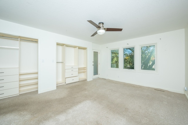 unfurnished bedroom featuring light colored carpet, baseboards, two closets, and ceiling fan