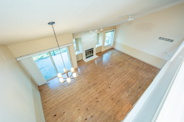 unfurnished living room featuring visible vents, a chandelier, a fireplace, rail lighting, and wood finished floors