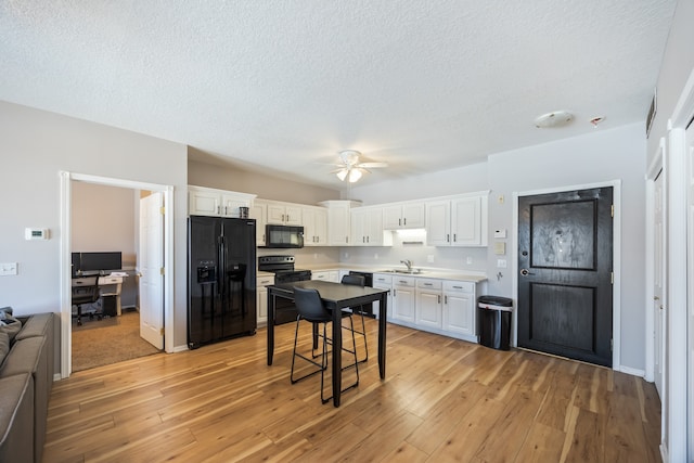 kitchen featuring a breakfast bar area, white cabinetry, black appliances, and light wood-type flooring