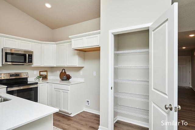 kitchen featuring white cabinets, wood-type flooring, stainless steel appliances, and lofted ceiling