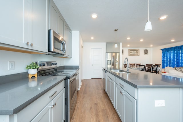 kitchen featuring sink, light hardwood / wood-style floors, stainless steel appliances, decorative light fixtures, and a kitchen island with sink