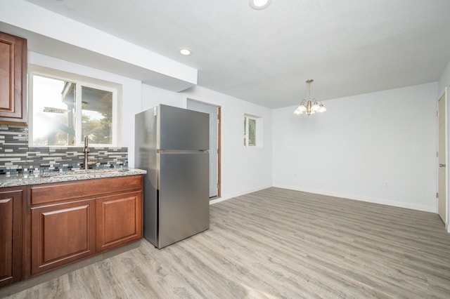 kitchen with sink, stainless steel fridge, backsplash, light stone counters, and light wood-type flooring