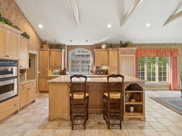 kitchen with stainless steel double oven, light brown cabinets, a center island, a kitchen bar, and light stone counters