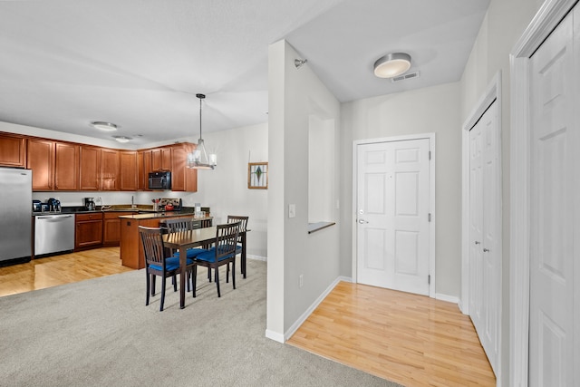 kitchen featuring appliances with stainless steel finishes, decorative light fixtures, light wood-type flooring, and an inviting chandelier