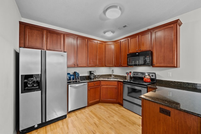 kitchen featuring light hardwood / wood-style floors, dark stone countertops, stainless steel appliances, and sink