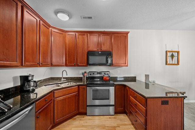 kitchen featuring kitchen peninsula, stainless steel appliances, dark stone countertops, sink, and light hardwood / wood-style floors