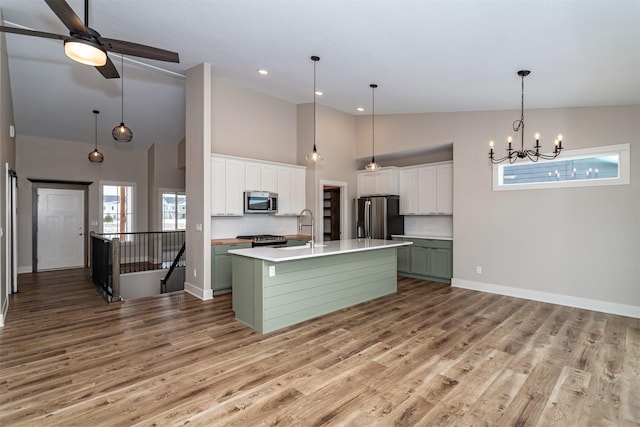 kitchen with stainless steel appliances, a kitchen island with sink, green cabinetry, ceiling fan with notable chandelier, and white cabinets