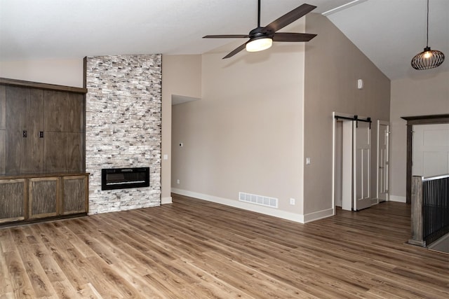 unfurnished living room featuring a barn door, hardwood / wood-style floors, a stone fireplace, ceiling fan, and lofted ceiling