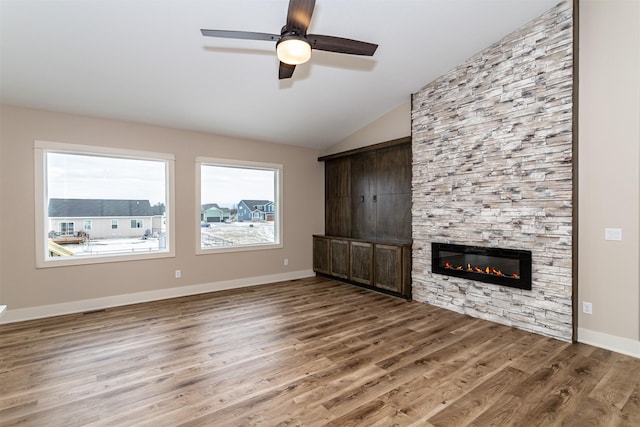 unfurnished living room with vaulted ceiling, a wealth of natural light, a stone fireplace, and hardwood / wood-style floors