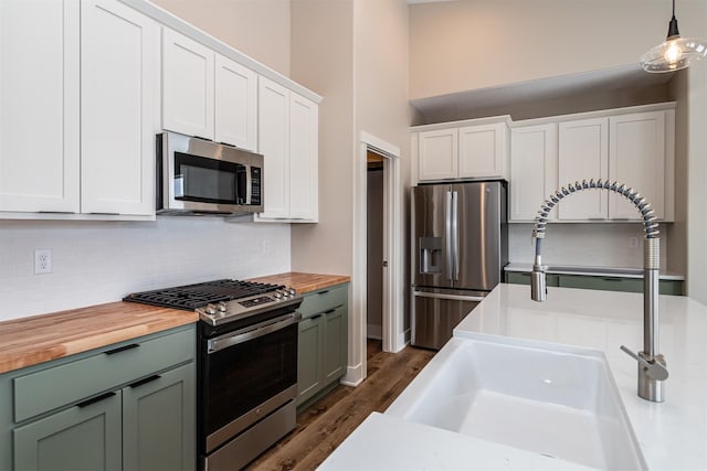 kitchen with decorative light fixtures, white cabinetry, appliances with stainless steel finishes, and butcher block counters