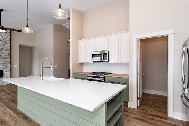 kitchen with pendant lighting, appliances with stainless steel finishes, white cabinetry, sink, and a kitchen island with sink