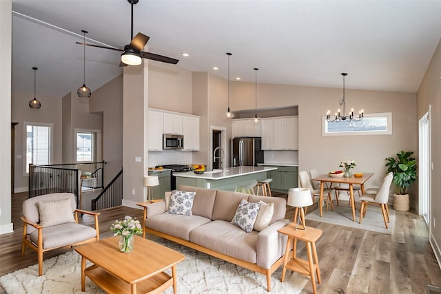 living room with ceiling fan with notable chandelier, sink, light hardwood / wood-style floors, and high vaulted ceiling