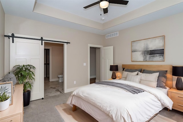 carpeted bedroom featuring ceiling fan, connected bathroom, a raised ceiling, and a barn door