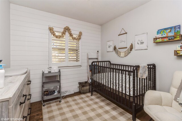 bedroom featuring wood walls, light hardwood / wood-style flooring, and a nursery area