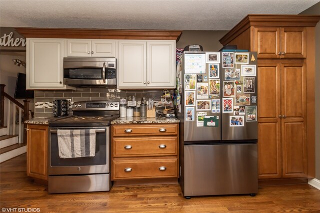 kitchen with appliances with stainless steel finishes, a textured ceiling, hardwood / wood-style flooring, and tasteful backsplash