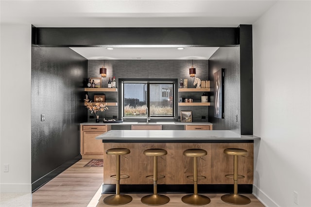 bar with light brown cabinetry, sink, and light hardwood / wood-style flooring