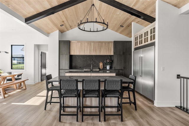 kitchen with vaulted ceiling with beams, a kitchen island, stainless steel built in refrigerator, a kitchen breakfast bar, and wooden ceiling